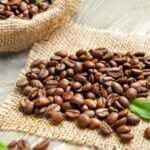 Frissen pörkölt Arabica kávészemek egy vászonzsákból kiömlve.