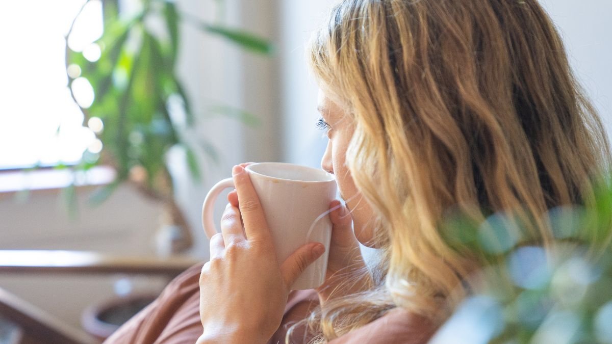 Egy nő kávét iszik, miközben a napfény átszűrődik az ablakon.