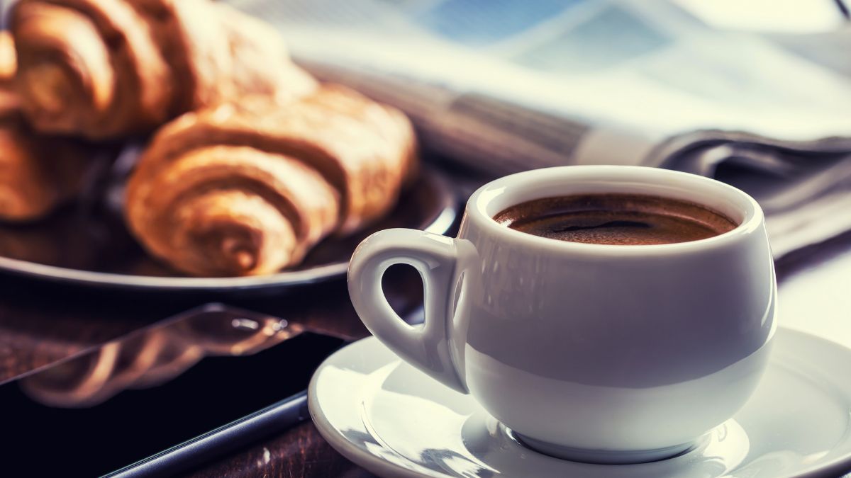 Egy csésze friss kávé mellett croissant és okostelefon található.