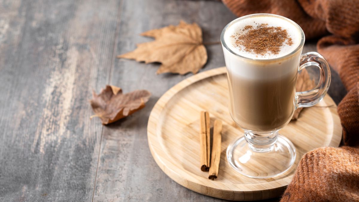 Egy üveg kávé tejhabbal, fahéjjal díszítve, fából készült tányéron.